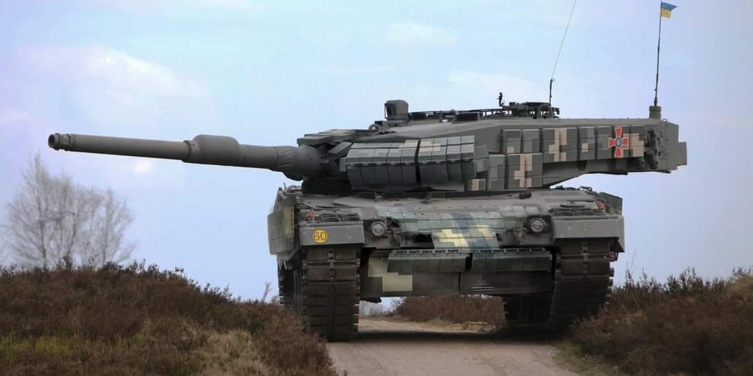 Grafika to fotomontaż – niemiecki czołg Leopard 2 osłonięty pancerzem reaktywnym Kontakt-1 w kamuflażu oraz ze znakiem rozpoznawczym Sił Zbrojnych Ukrainy.